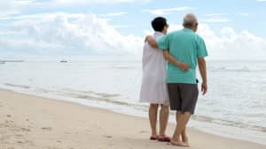 Asian senior couple walking together on beach by the sea